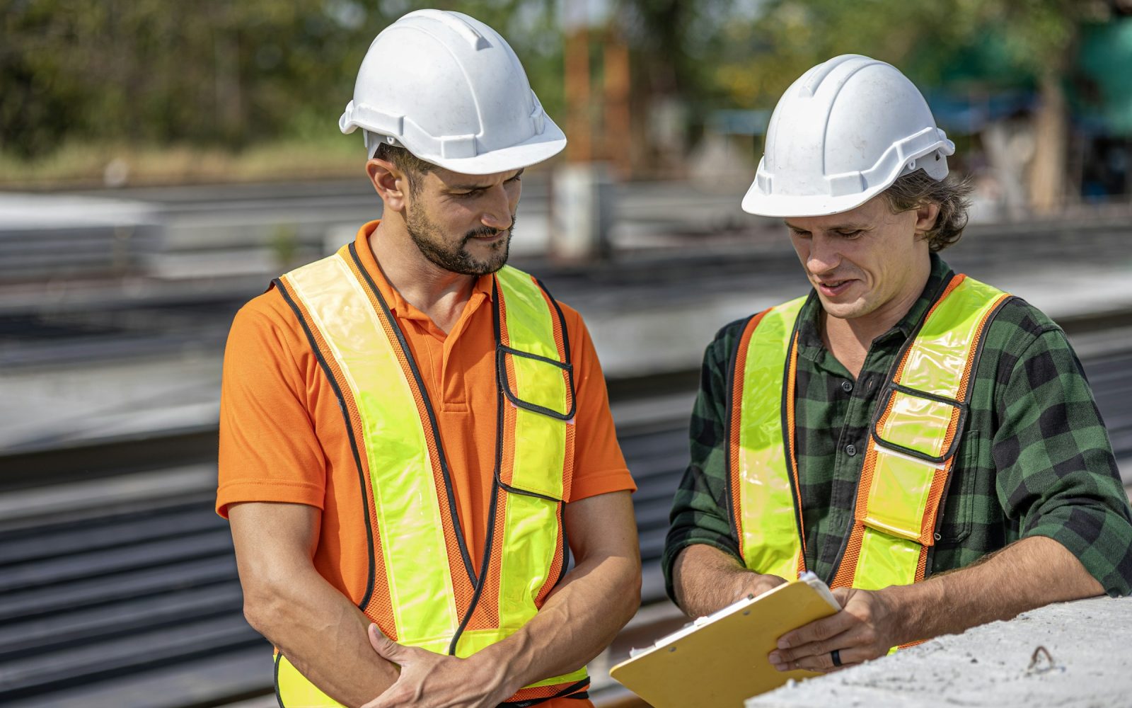 Two construction professionals in safety equipment reviewing a project document on site.